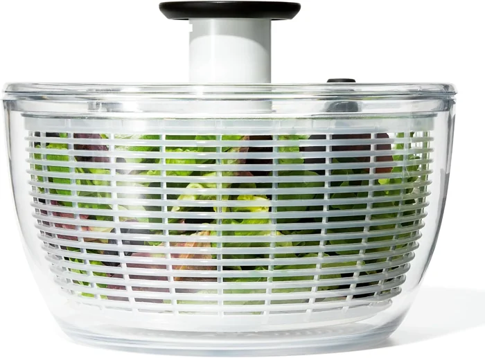 OXO Good Grips salad spinner with clear bowl, white basket of greens and black pump knob